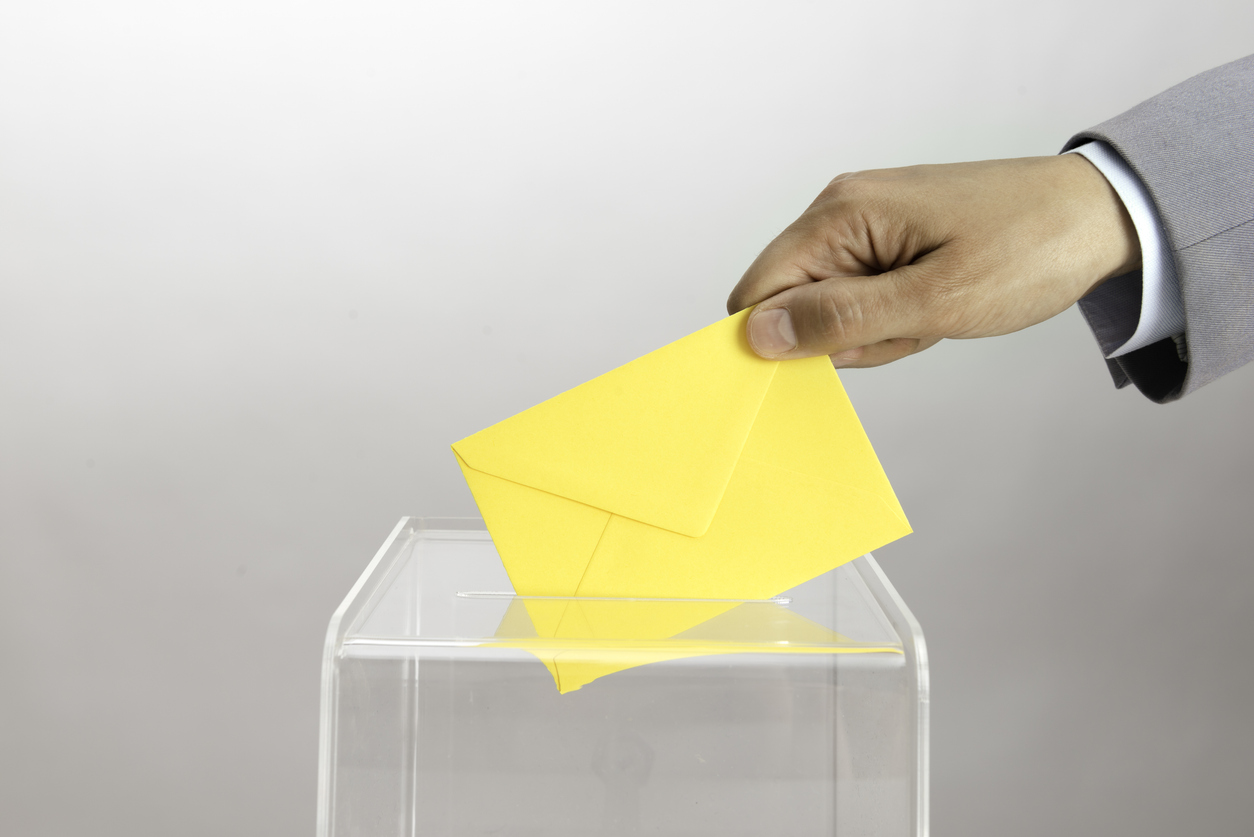 Main déposant une enveloppe jaune dans une urne transparente